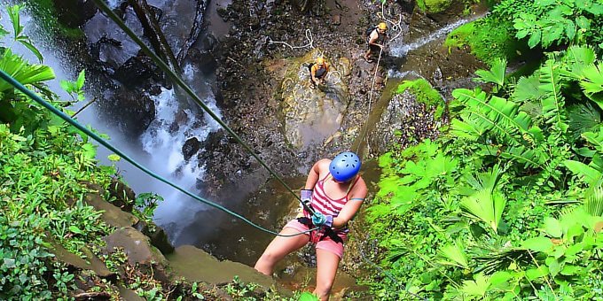 A woman rappels down the face of a waterfall on a canyoning adventure tour